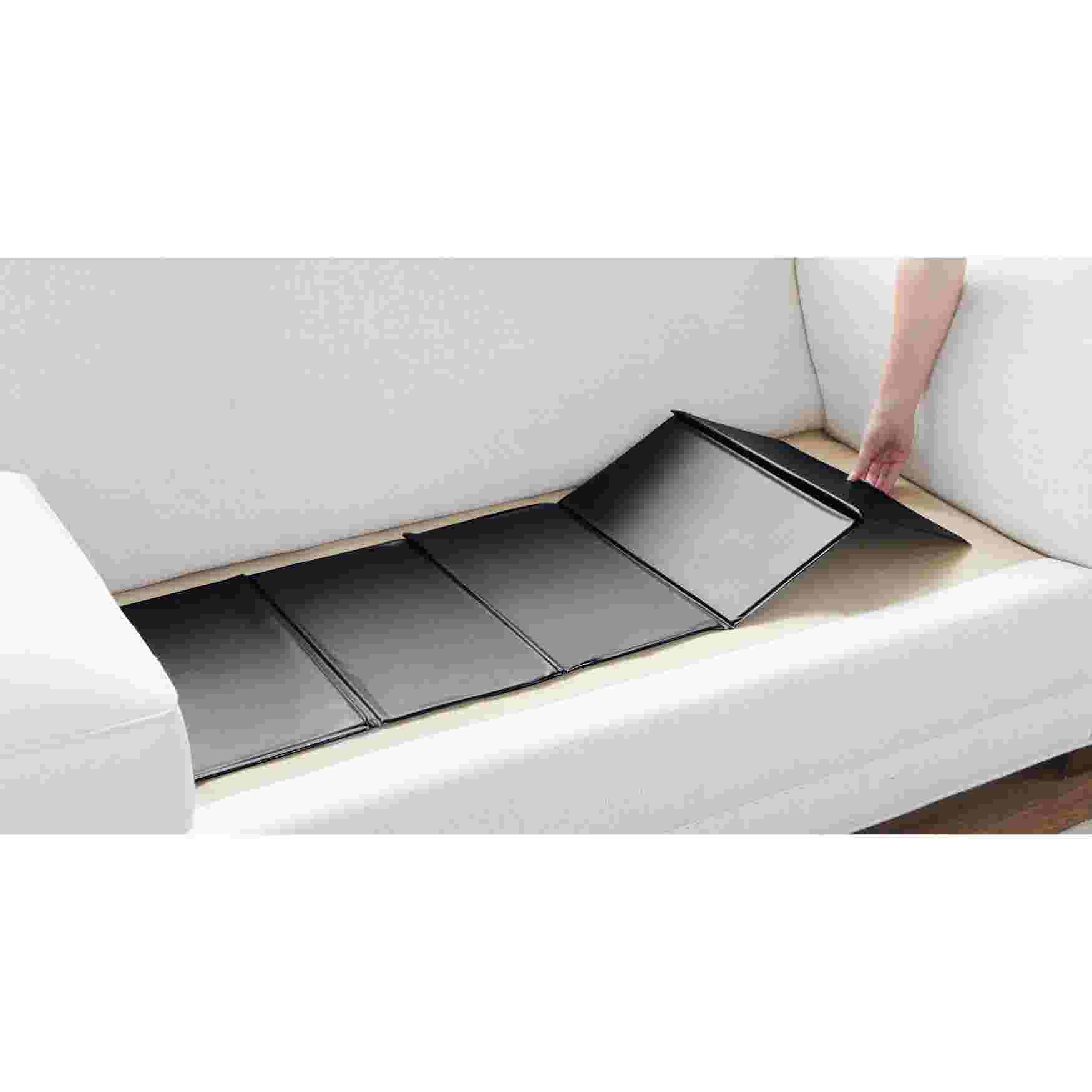 A person placing a black sofa cushion support on a white couch.